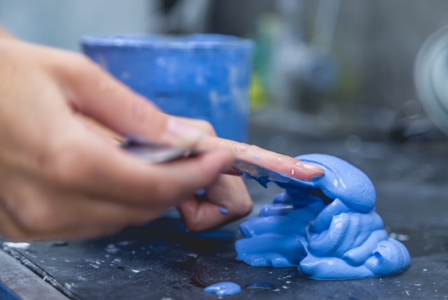 Tandprotheticus bewerkt blauwe kunsthars voor het maken van een gebitsprothese in de tandtechnische werkplaats