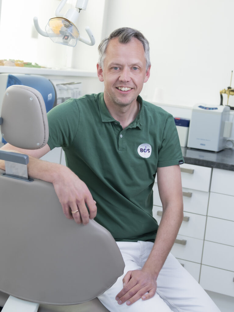 Professionele tandprotheticus in groene polo in moderne tandheelkundige behandelkamer met tandartsstoel