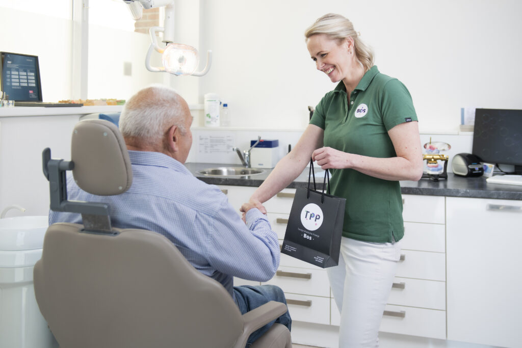 Tandprotheticus in gesprek met oudere patiënt in tandheelkundige behandelstoel tijdens consultatie