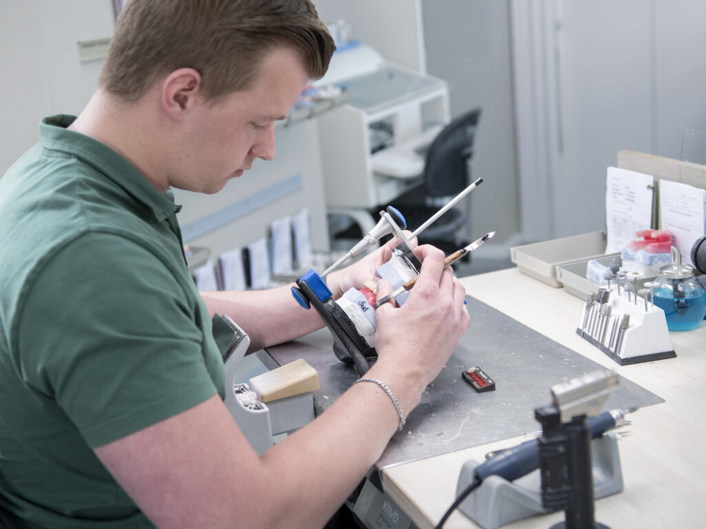 Tandprotheticus bewerkt tandprothese met precisie-instrument in moderne werkplaats